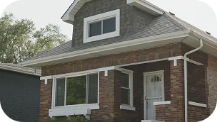 A small brick house with a covered front porch, white trim, and a gabled roof, pictured on a clear day.