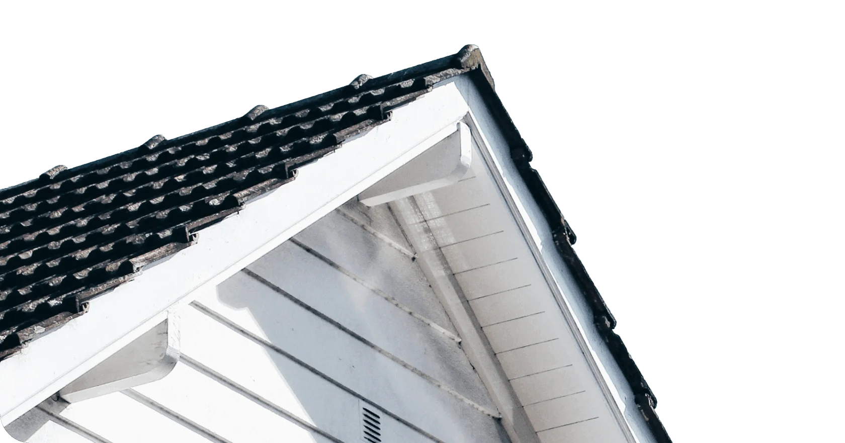 Close-up view of a house roof with dark shingles and white wooden siding, photographed at an upward angle against a blank background.