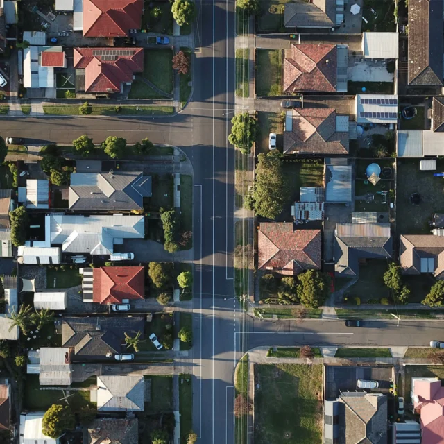 Aerial view of a suburban neighborhood with houses, intersecting roads, driveways, and trees.