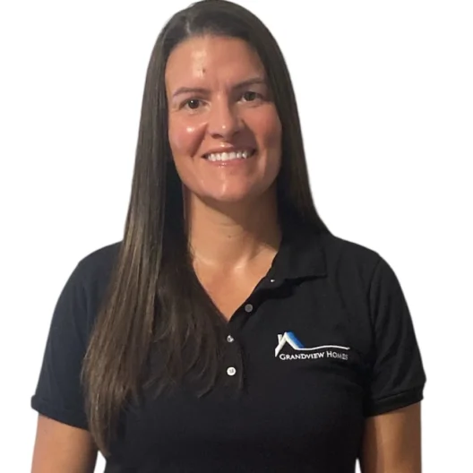 A woman with long brown hair wearing a black Grandview Homes polo shirt stands and smiles against a white background.