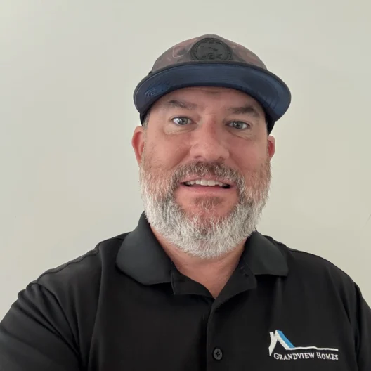 A man with a beard wears a black Grandview Homes polo shirt and a dark cap, standing in front of a plain light-colored background.