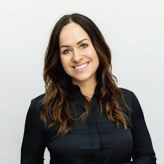 Woman with long brown hair and a black shirt smiling in front of a plain white background.
