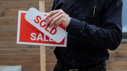 A person places a "SOLD" sign over a "FOR SALE" sign, indicating a sale has been completed.
