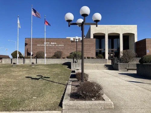 City Hall building in Chicago Heights, Illinois, with three flagpoles and globe street lamps along a concrete walkway.
