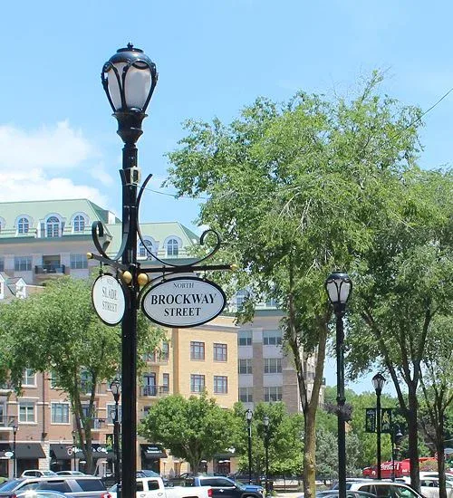 Street signs for Slade Street and North Brockway Street on a black lamp post, with trees and an apartment building in the background on a sunny day.